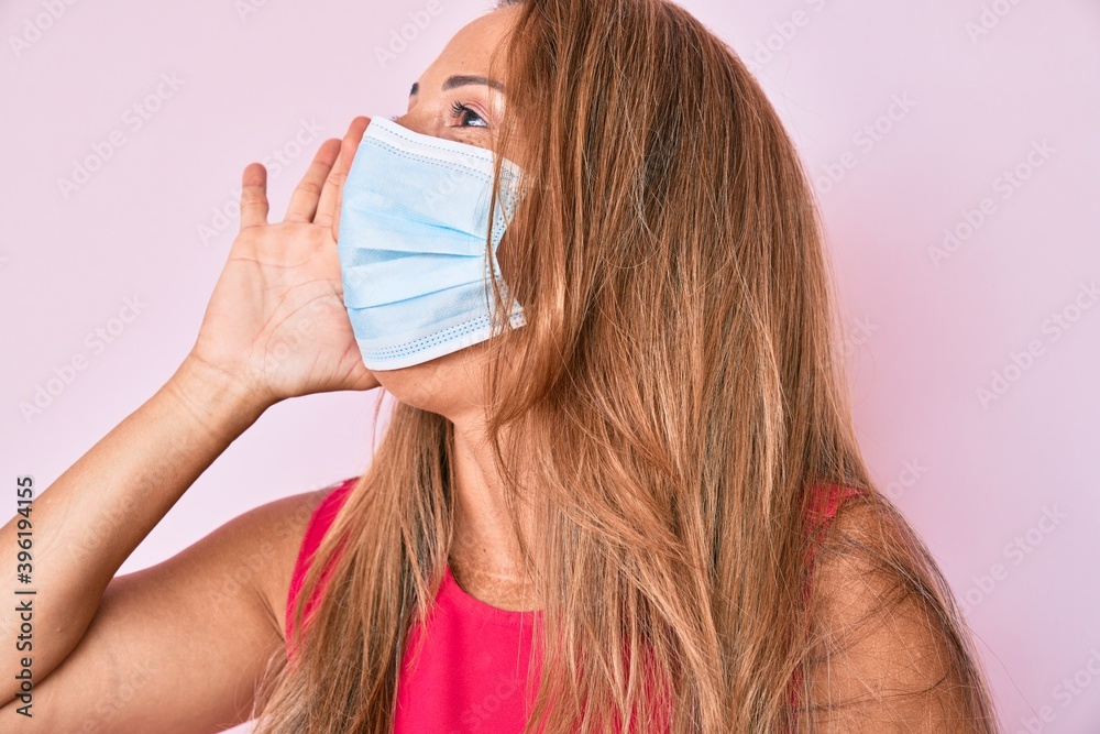 Middle age hispanic woman wearing medical mask shouting and screaming loud to side with hand on mouth. communication concept. Middle age hispanic woman wearing medical mask shouting and screaming loud to side with hand on mouth. communication concept.