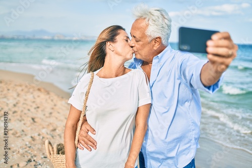 Middle age hispanic couple making selfie by the smartphone kissing at the beach.