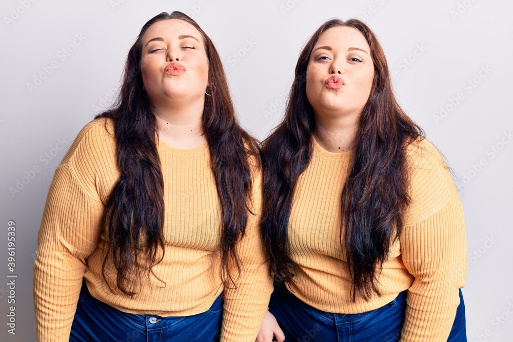 Young plus size twins wearing casual clothes looking at the camera blowing a kiss on air being lovely and sexy. love expression. Young plus size twins wearing casual clothes looking at the camera blowing a kiss on air being lovely and sexy. love expression.