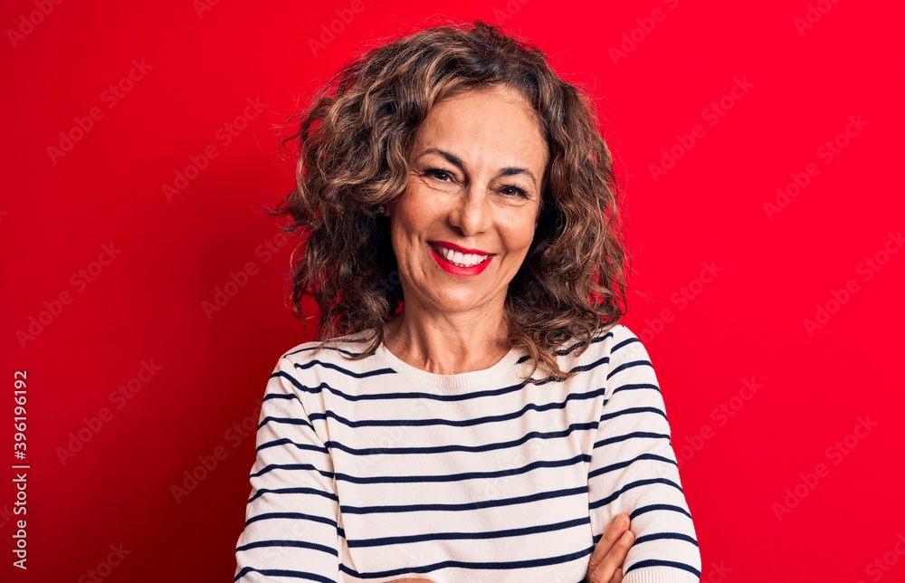 Middle age beautiful brunette woman wearing striped t-shirt standing over red background happy face smiling with crossed arms looking at the camera. Positive person. Middle age beautiful brunette woman wearing striped t-shirt standing over red background happy face smiling with crossed arms looking at the camera. Positive person.