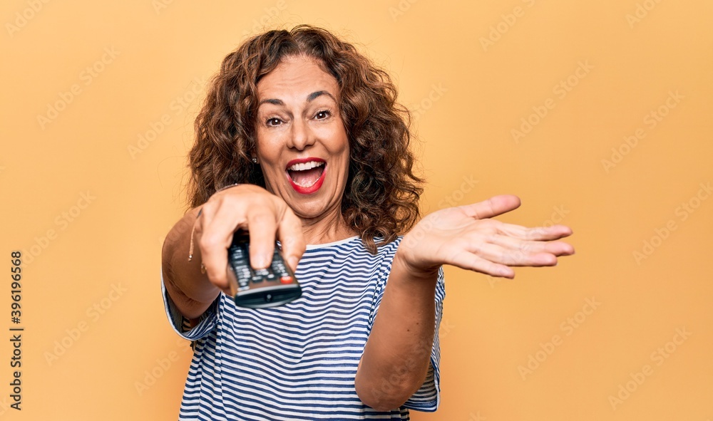 Middle age beautiful woman changing tv channel using television remote control celebrating achievement with happy smile and winner expression with raised hand Middle age beautiful woman changing tv channel using television remote control celebrating achievement with happy smile and winner expression with raised hand