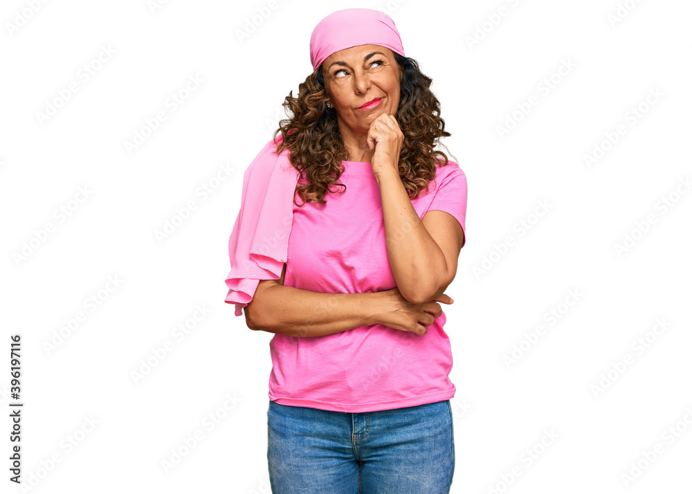 Middle age hispanic woman wearing breast cancer support pink scarf serious face thinking about question with hand on chin, thoughtful about confusing idea Middle age hispanic woman wearing breast cancer support pink scarf serious face thinking about question with hand on chin, thoughtful about confusing idea