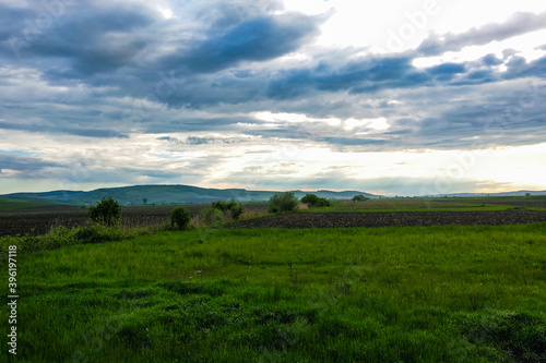 Dramatic sky and green meadows, in the distance one can see mountains, nature background.