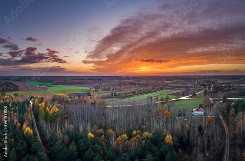 Picturesque autumn scene with colorful trees in countryside. Vibrant colors in sky at sunset.