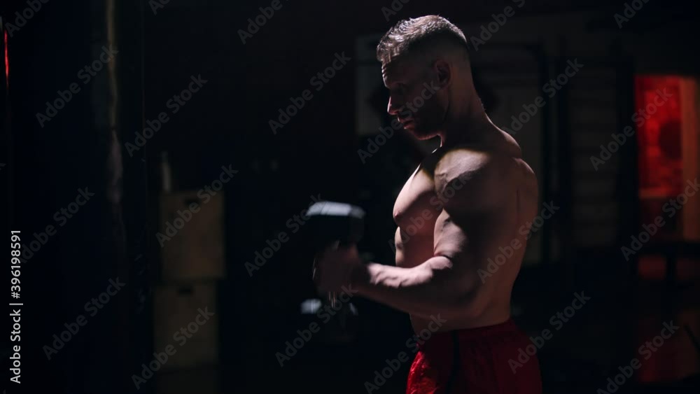 Strong man pumping his biceps with dumbbells Strong man pumping his biceps with dumbbells