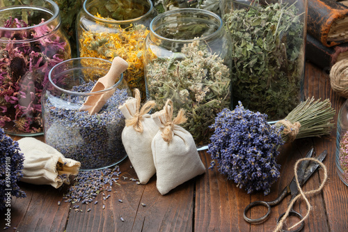 Glass jars of dry different medicinal herbs, aromatic sachets, bunches of dry lavender on table. Alternative medicine.