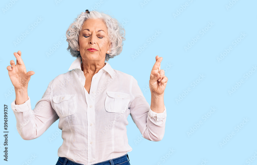 Senior grey-haired woman wearing casual clothes gesturing finger crossed smiling with hope and eyes closed. luck and superstitious concept. Senior grey-haired woman wearing casual clothes gesturing finger crossed smiling with hope and eyes closed. luck and superstitious concept.