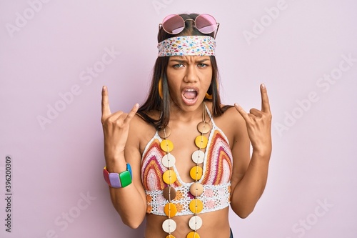 Beautiful hispanic woman wearing bohemian and hippie style shouting with crazy expression doing rock symbol with hands up. music star. heavy concept.