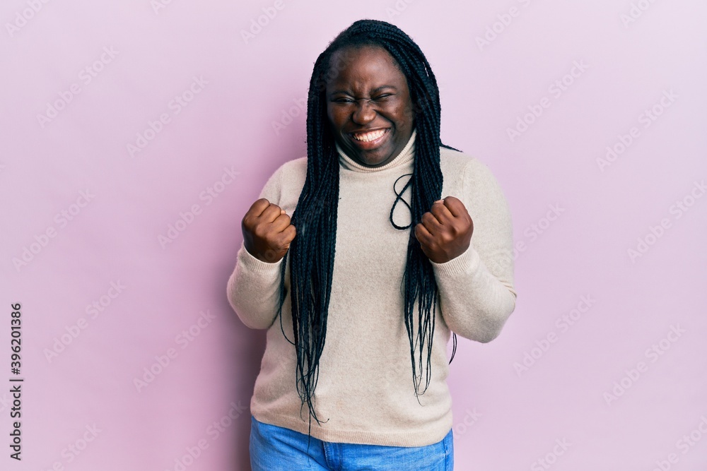 Young black woman with braids wearing casual winter sweater excited for success with arms raised and eyes closed celebrating victory smiling. winner concept. Young black woman with braids wearing casual winter sweater excited for success with arms raised and eyes closed celebrating victory smiling. winner concept.