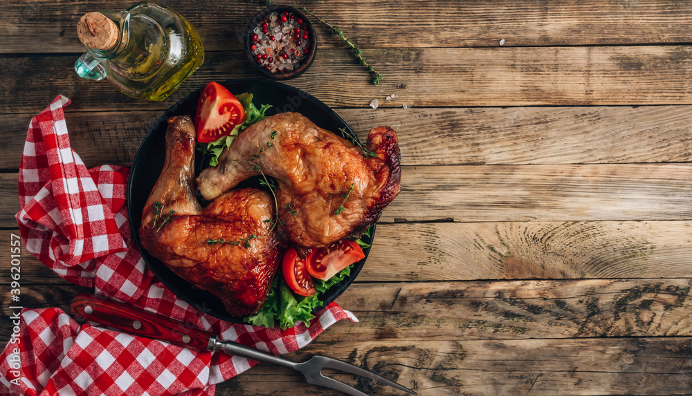Naklejka premium Roasted chicken legs with vegetables and herbs on black plate over rustic wooden background