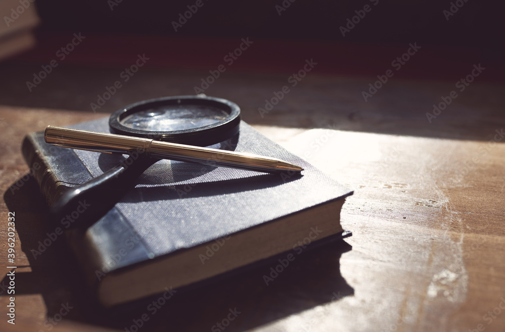 Old book with magnifying glass and pen on table Old book with magnifying glass and pen on table