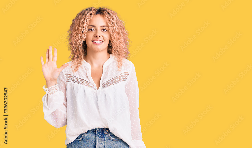 Young blonde woman with curly hair wearing elegant summer shirt showing and pointing up with fingers number five while smiling confident and happy. Young blonde woman with curly hair wearing elegant summer shirt showing and pointing up with fingers number five while smiling confident and happy.