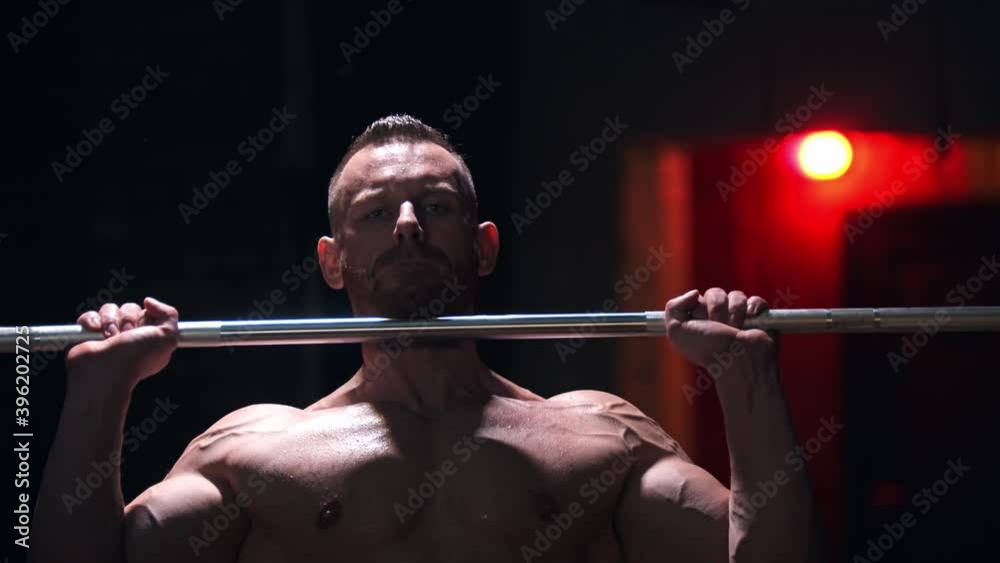 Tough shirtless man covered in sweat standing in the gym - pulling up a heavy bar with an effort and screaming Tough shirtless man covered in sweat standing in the gym - pulling up a heavy bar with an effort and screaming