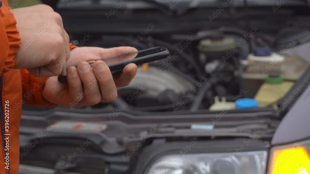 Close-up of a hand using a phone on a background of a car with a flashing alarm Close-up of a hand using a phone on a background of a car with a flashing alarm