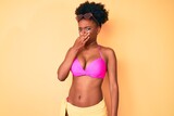Young african american woman wearing bikini smelling something stinky and disgusting, intolerable smell, holding breath with fingers on nose. bad smell