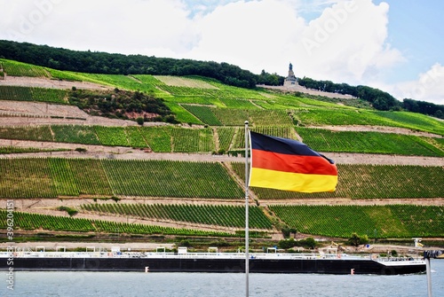 Bingen Am Rhein, Germany: View of the Rhein River with a boat, German flag and vineyards. Niederwalddenkmal, Germania statue, a monument for the German reunification, in Rudeshiem.  photo