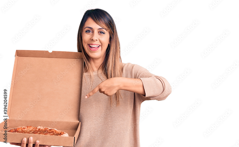 Young beautiful woman holding delivery cardboard box with pizza smiling happy pointing with hand and finger Young beautiful woman holding delivery cardboard box with pizza smiling happy pointing with hand and finger