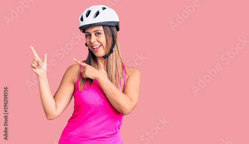 Young beautiful woman wearing bike helmet smiling and looking at the camera pointing with two hands and fingers to the side.