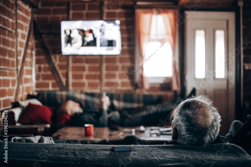 Elderly man watching tv  sitting on a sofa. Back view
