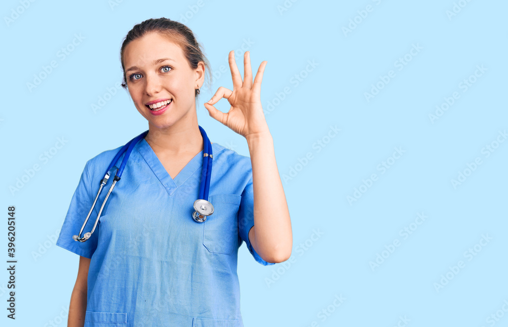 Young beautiful blonde woman wearing doctor uniform and stethoscope smiling positive doing ok sign with hand and fingers. successful expression. Young beautiful blonde woman wearing doctor uniform and stethoscope smiling positive doing ok sign with hand and fingers. successful expression.