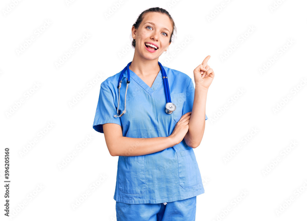 Young beautiful blonde woman wearing doctor uniform and stethoscope with a big smile on face, pointing with hand and finger to the side looking at the camera. Young beautiful blonde woman wearing doctor uniform and stethoscope with a big smile on face, pointing with hand and finger to the side looking at the camera.