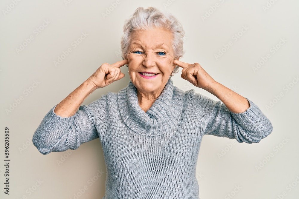 Senior grey-haired woman covering ears with finger smiling with a happy and cool smile on face. showing teeth. Senior grey-haired woman covering ears with finger smiling with a happy and cool smile on face. showing teeth.