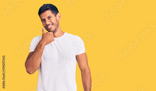 Young latin man wearing casual clothes looking confident at the camera smiling with crossed arms and hand raised on chin. thinking positive.
