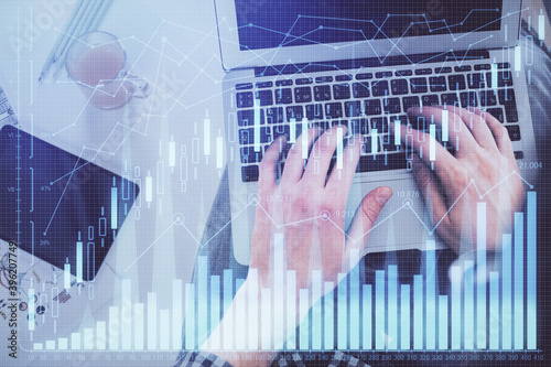 Double exposure of man's hands typing over laptop keyboard and forex chart hologram drawing. Top view. Financial markets concept. © peshkova