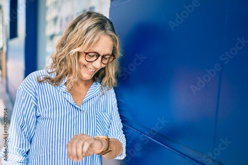 Fototapeta Middle age caucasian woman smiling happy looking watch standing at the city