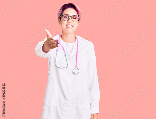 Young beautiful woman with pink hair wearing doctor uniform smiling friendly offering handshake as greeting and welcoming. successful business. © Krakenimages.com