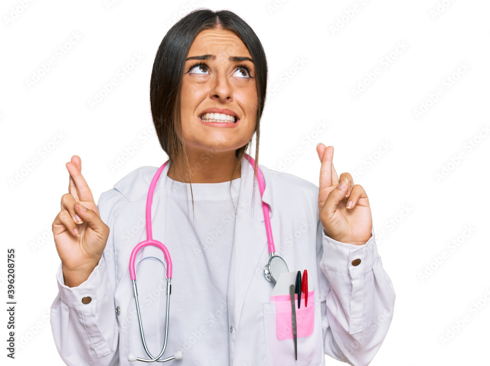 Beautiful hispanic woman wearing doctor uniform and stethoscope gesturing finger crossed smiling with hope and eyes closed. luck and superstitious concept. Beautiful hispanic woman wearing doctor uniform and stethoscope gesturing finger crossed smiling with hope and eyes closed. luck and superstitious concept.