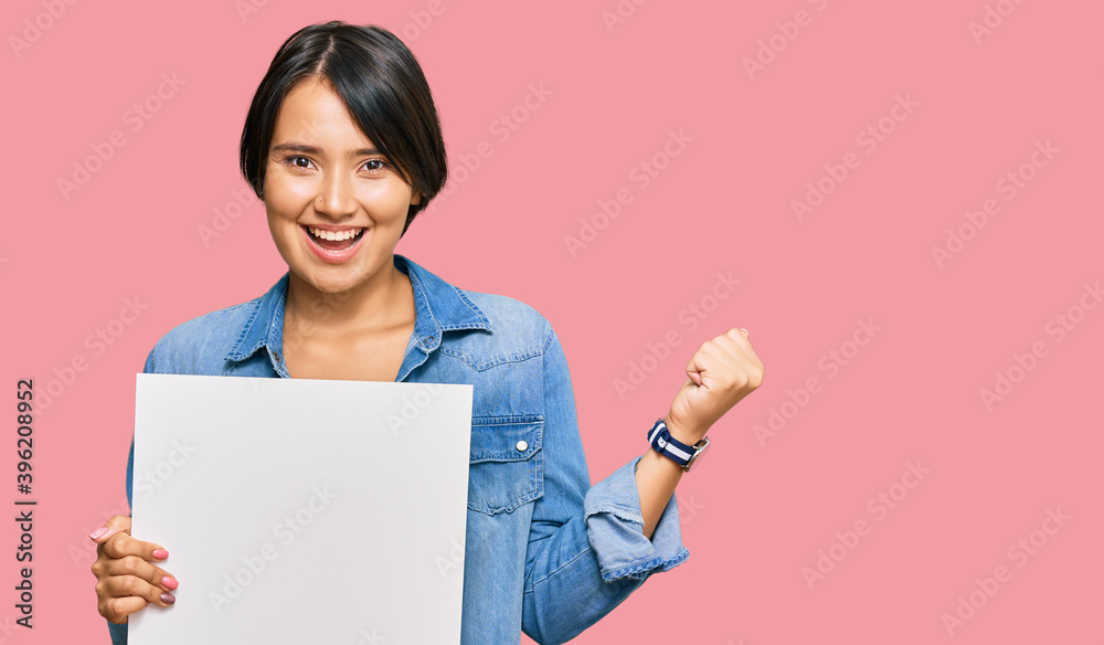Beautiful young woman with short hair holding blank empty banner screaming proud, celebrating victory and success very excited with raised arms