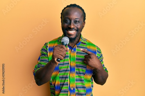 Handsome young black man singing song using microphone smiling happy pointing with hand and finger