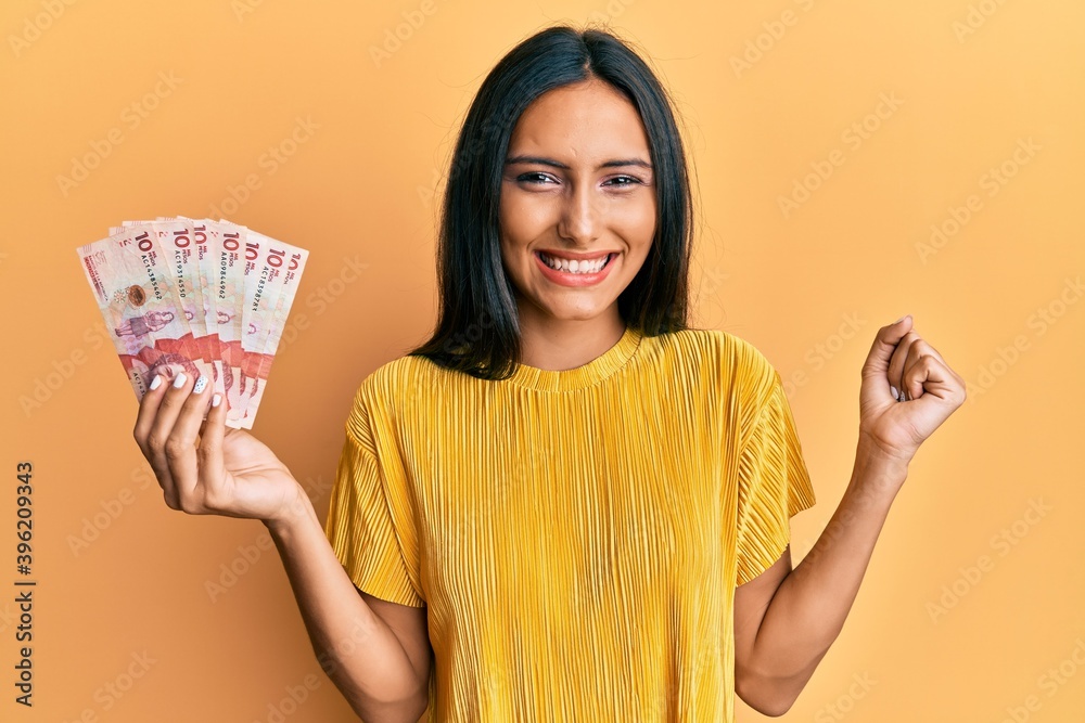 Young brunette woman holding 10 colombian pesos banknotes screaming proud, celebrating victory and success very excited with raised arm Young brunette woman holding 10 colombian pesos banknotes screaming proud, celebrating victory and success very excited with raised arm