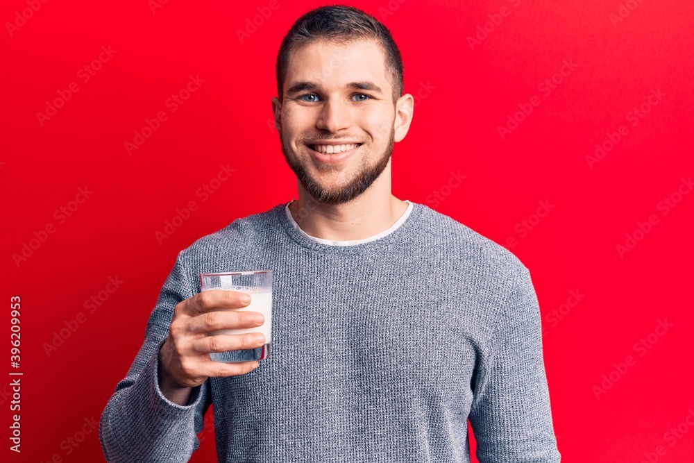 Young handsome man drinking glass of milk looking positive and happy standing and smiling with a confident smile showing teeth Young handsome man drinking glass of milk looking positive and happy standing and smiling with a confident smile showing teeth