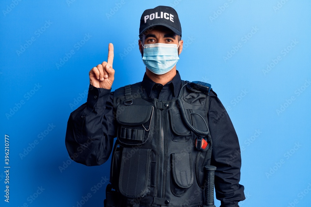 Young hispanic man wearing police uniform and medical mask smiling with an idea or question pointing finger up with happy face, number one Young hispanic man wearing police uniform and medical mask smiling with an idea or question pointing finger up with happy face, number one