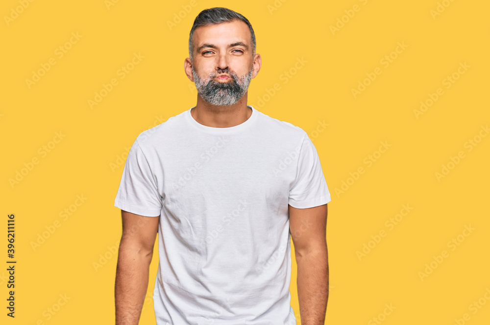 Middle age handsome man wearing casual white tshirt puffing cheeks with funny face. mouth inflated with air, crazy expression. Middle age handsome man wearing casual white tshirt puffing cheeks with funny face. mouth inflated with air, crazy expression.