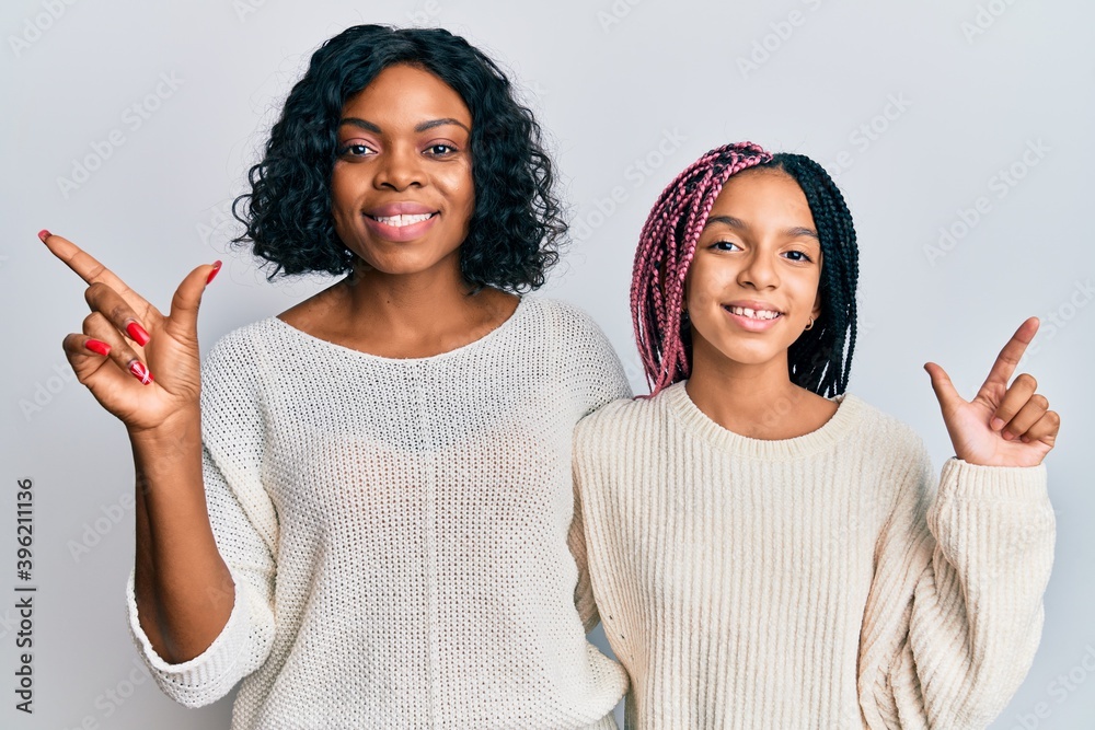 Beautiful african american mother and daughter wearing casual clothes and hugging cheerful with a smile on face pointing with hand and finger up to the side with happy and natural expression Beautiful african american mother and daughter wearing casual clothes and hugging cheerful with a smile on face pointing with hand and finger up to the side with happy and natural expression