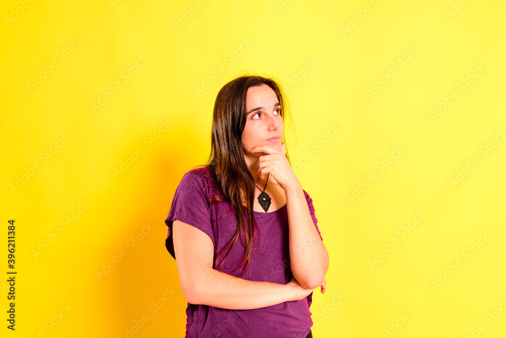 Young long-haired woman with doubtful and pensive expression and gesture, isolated on yellow background.