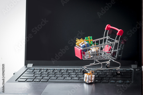 Trolley with shopping bags, Christmas decoration items and gift box on laptop keyboard. Online shopping on Xmas, electronic commerce business and buying goods from seller over the internet concept for