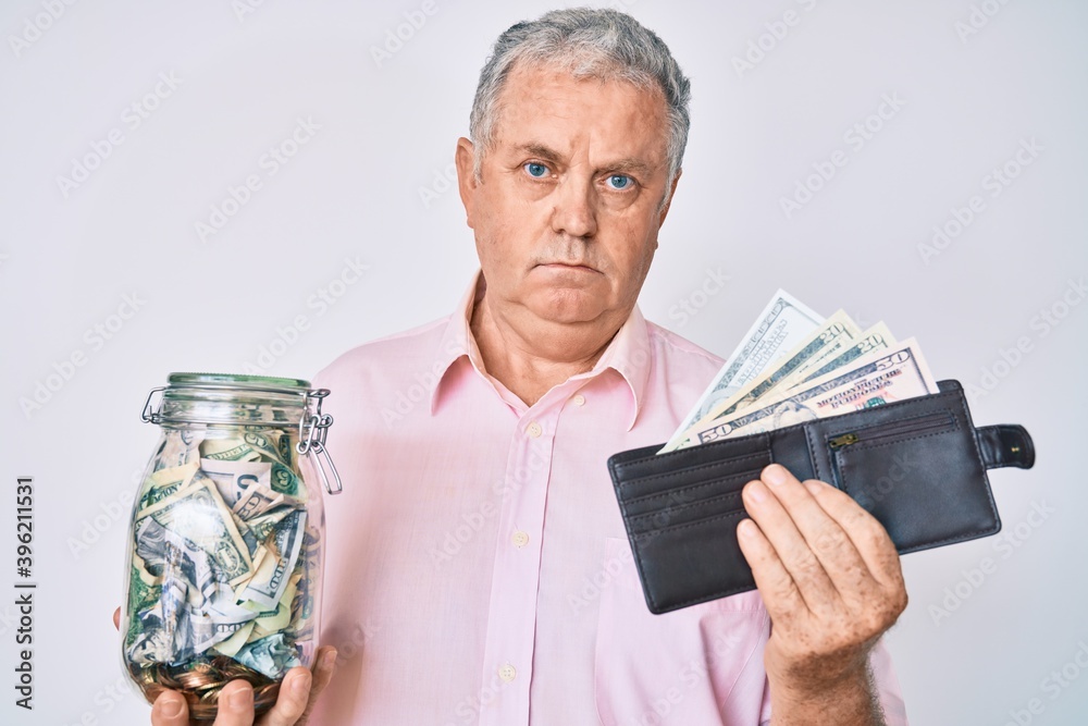 Senior grey-haired man holding wallet with dollars and jar with savings relaxed with serious expression on face. simple and natural looking at the camera. Senior grey-haired man holding wallet with dollars and jar with savings relaxed with serious expression on face. simple and natural looking at the camera.