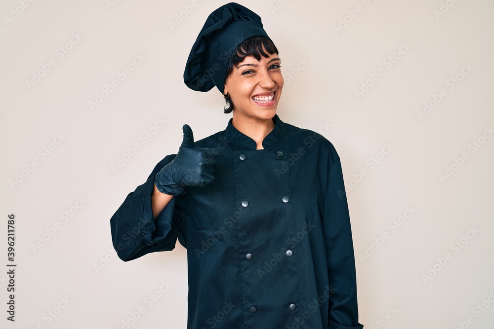 Beautiful brunettte woman wearing professional cook uniform doing happy thumbs up gesture with hand. approving expression looking at the camera showing success. Beautiful brunettte woman wearing professional cook uniform doing happy thumbs up gesture with hand. approving expression looking at the camera showing success.