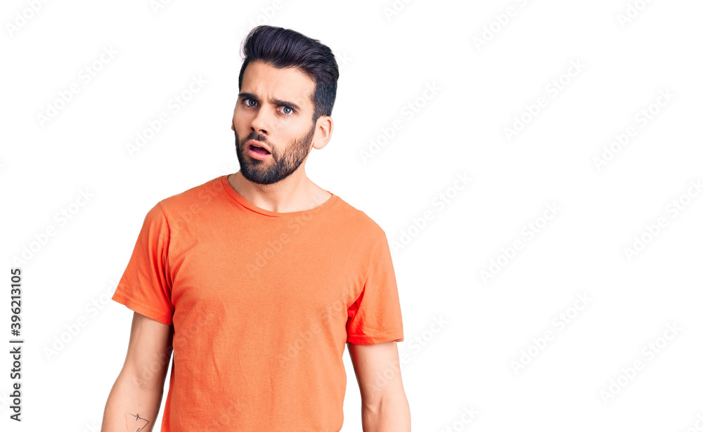 Fototapeta premium Young handsome man with beard wearing casual t-shirt in shock face, looking skeptical and sarcastic, surprised with open mouth
