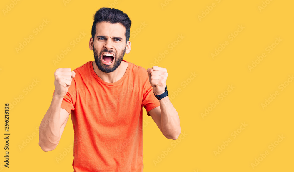Young handsome man with beard wearing casual t-shirt angry and mad raising fists frustrated and furious while shouting with anger. rage and aggressive concept. Young handsome man with beard wearing casual t-shirt angry and mad raising fists frustrated and furious while shouting with anger. rage and aggressive concept.