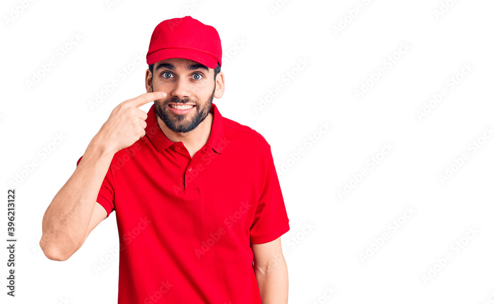 Young handsome man with beard wearing delivery uniform pointing with hand finger to face and nose, smiling cheerful. beauty concept
