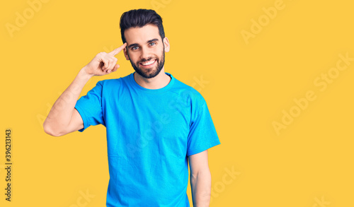 Young handsome man with beard wearing casual t-shirt smiling pointing to head with one finger, great idea or thought, good memory