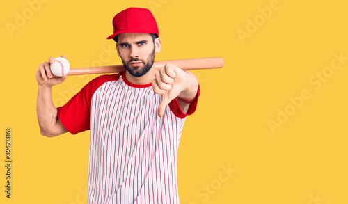 Young handsome man with beard playing baseball holding bat and ball with angry face  negative sign showing dislike with thumbs down  rejection concept