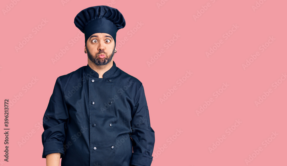 Young hispanic man wearing cooker uniform making fish face with lips, crazy and comical gesture. funny expression. Young hispanic man wearing cooker uniform making fish face with lips, crazy and comical gesture. funny expression.
