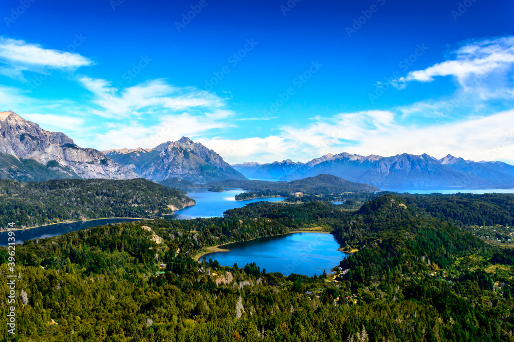Beautiful lake landscape in the middle of mountains surrounded by pine trees and rocks everywhere. Very sunny day in the mountain of Bariloche. Green foliage and huge rocks.