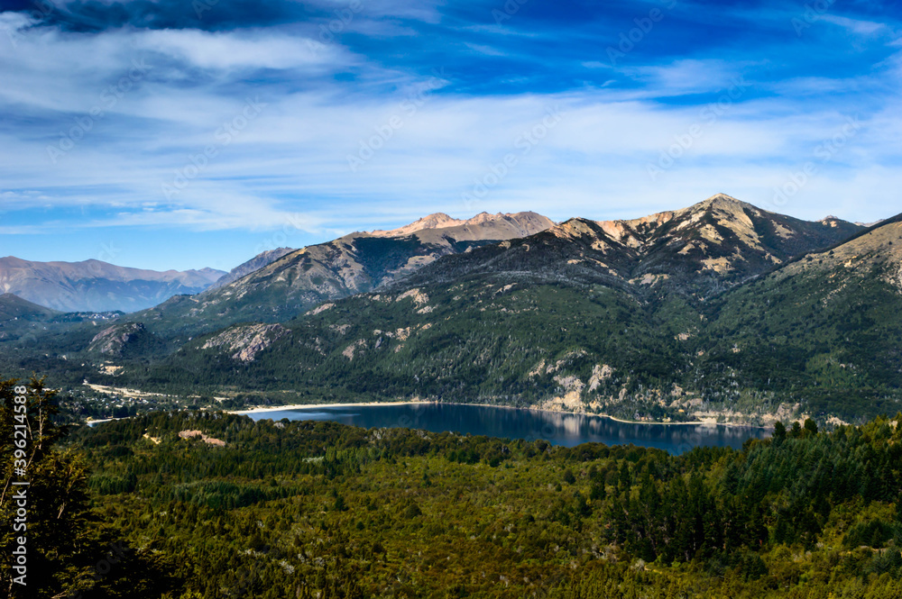 Beautiful lake landscape in the middle of mountains surrounded by pine trees and rocks everywhere. Very sunny day in the mountain of Bariloche. Green foliage and huge rocks.